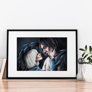 Op de afbeelding: Ingelijste kunstdruk met een romantische illustratie van twee figuren met donker haar en blauwe accenten, die elkaar aankijken. Het kunstwerk staat in een zwart frame, op een houten oppervlak. Een witte vaas met groen is ook zichtbaar.