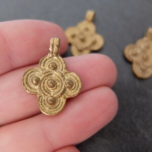 May include: Close-up of several small, gold-colored pendants. The pendants have a four-petal flower design with concentric circles and small, raised dots. The pendants are likely made of metal and are suitable for jewelry making.
