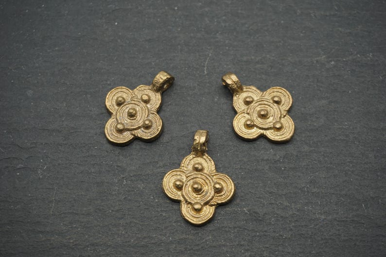 May include: Three antique gold-colored pendants with a four-petal flower design. Each pendant has a loop at the top for hanging. The pendants are made of metal and have a textured surface.