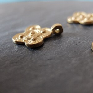 May include: Close-up of several small, gold-colored cloud-shaped pendants. Each pendant has a loop for hanging and a detailed, swirling design. The pendants are on a dark gray surface.