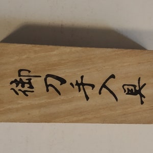 以下が含まれることがあります： 黒い文字が刻まれた長方形の木製ブロック。木材は明るい茶色で、木目が見えます。文字は縦書きです。