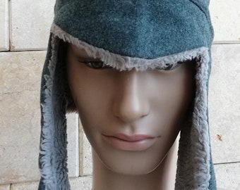 Może przedstawiać: Tealowa zimowa czapka z nausznikami i podszewką z imitacji futra. Czapka wykonana jest z miękkiego, teksturowanego materiału i ma chronić przed zimnem. Nauszniki sięgają do ramion.
