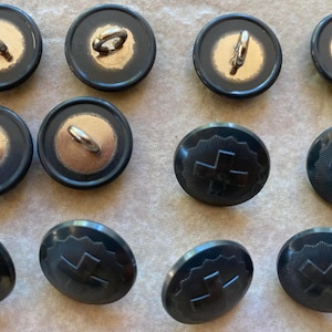 Puede incluir: Doce botones de plástico negro con un centro dorado. Algunos botones tienen un bucle en la parte superior, mientras que otros tienen un diseño de cruz.