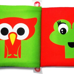 May include: A green and red fabric book with a red owl and a green frog on the front. The book has yellow, orange, and pink tabs.