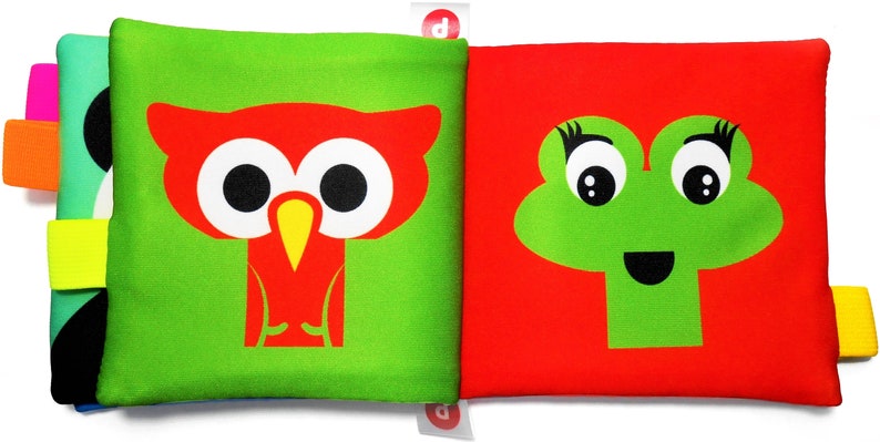 May include: A green and red fabric book with a red owl and a green frog on the front. The book has yellow, orange, and pink tabs.