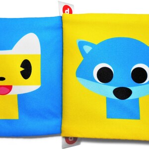 May include: A yellow and blue baby book with a yellow cat face on one side and a blue cat face on the other side. The book has colorful fabric tabs on the sides.