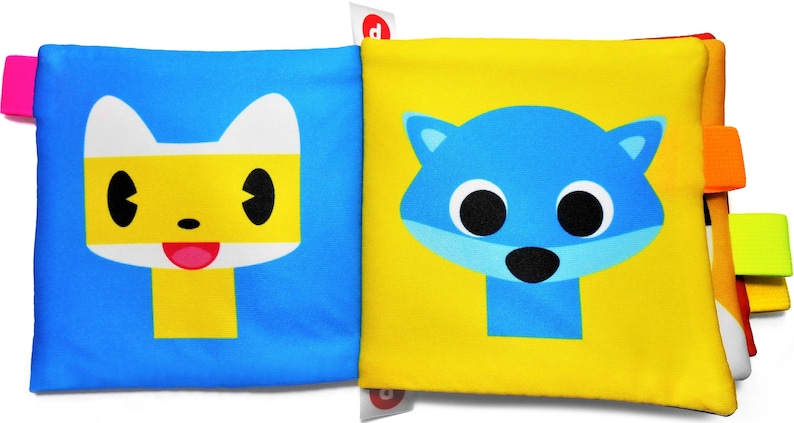 May include: A yellow and blue baby book with a yellow cat face on one side and a blue cat face on the other side. The book has colorful fabric tabs on the sides.