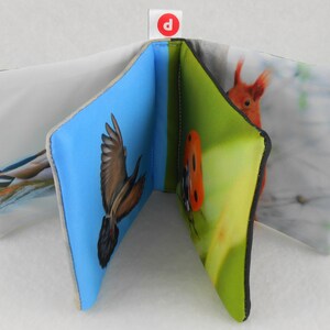 May include: A soft, fabric book for babies and toddlers with colorful images of a bird, a ladybug, a squirrel, and a bird in flight. The book has a blue, green, and white background.