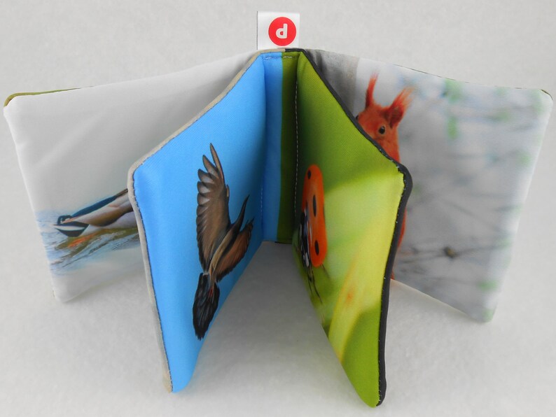 May include: A soft, fabric book for babies and toddlers with colorful images of a bird, a ladybug, a squirrel, and a bird in flight. The book has a blue, green, and white background.