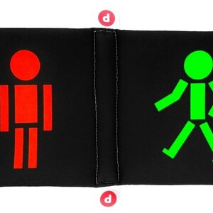 May include: A black and white pillow with a red stick figure on one side and a green stick figure walking on the other side.