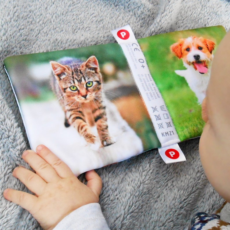 May include: A soft book for babies with a cat and a dog on the cover. The book has a label that says "P CE 0+ Made in Poland" and washing instructions.