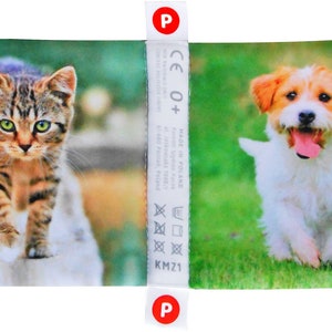 May include: A colorful fabric panel with a brown tabby cat walking on a white surface and a white and brown dog running on green grass. The panel has a white label with the text "CE 0+ Made in Poland" and washing instructions.