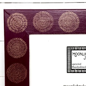 May include: A burgundy picture frame with a gold floral design. The frame has a white mat and a white background. The text "MOONLIGHT" is visible in the lower right corner of the image.
