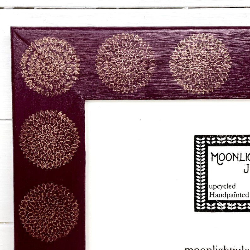 May include: A burgundy picture frame with a gold floral design. The frame has a white mat and a white background. The text "MOONLIGHT" is visible in the lower right corner of the image.