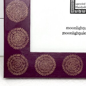 May include: A purple picture frame with a gold floral design. The frame has a white mat and the text "upcycled Handpainted moonlightjule moonlightjule" is printed on the mat.