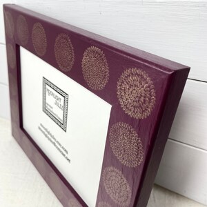 May include: A deep purple picture frame with a gold floral pattern around the edge. The frame is made of wood and has a matte finish. The text "Moonlight Jules" is printed on the inside of the frame.