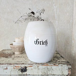 Può includere: Una tazza di ceramica bianca con manico nero e la scritta "But First, Coffee" in nero, in grassetto. La tazza è appoggiata su una superficie bianca.