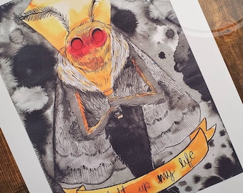 Könnte beinhalten: Ein Aquarellbild eines Nachtfalters mit großen, gefiederten Antennen und roten Augen. Der Falter hält ein kleines, leuchtendes Licht in seinen Vorderbeinen. Der Hintergrund ist dunkelgrau mit weißen und gelben Akzenten. Der Text "You light up my life" ist auf einem gelben Band geschrieben.