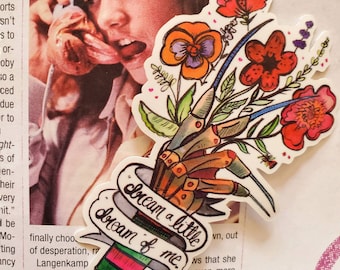 May include: A sticker featuring a Freddy Krueger-inspired hand holding a bouquet of colorful flowers. The hand is wearing a glove with sharp blades. The sticker has the text "Dream a little dream of me."