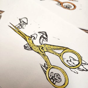 May include: A pair of gold scissors with a whimsical design featuring mushrooms. The scissors are open and the handles are shaped like mushrooms.