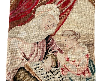 May include: A vintage needlepoint pillow depicting a woman and a child. The woman is wearing a pink dress and a white cap. The child is wearing a pink dress and has blonde hair. The pillow is framed in a brown border.