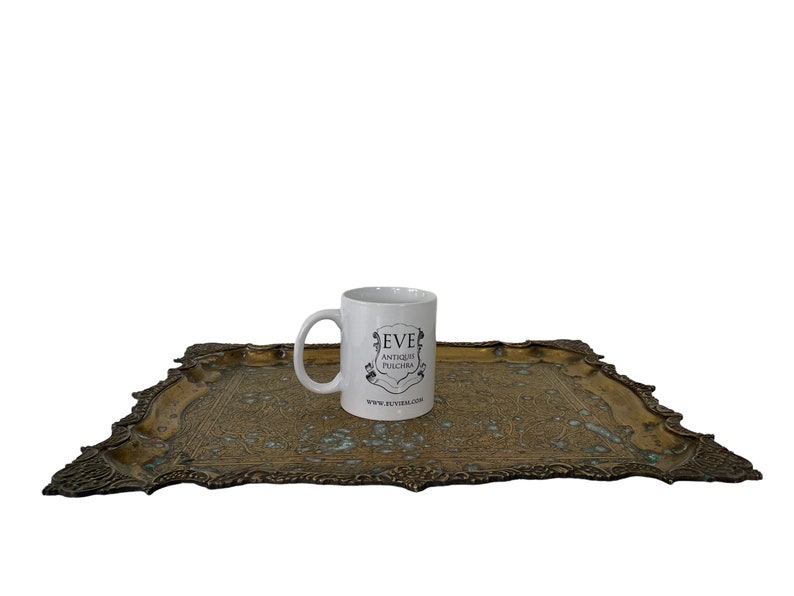 Puede incluir: Una taza de cer&aacute;mica blanca con un logotipo negro que dice "Eve Antique Pushcha" y una direcci&oacute;n de sitio web en una bandeja de metal dorado con un dise&ntilde;o ornamentado.
