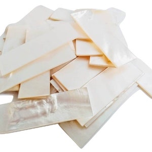 May include: A pile of white mother of pearl shell inlay sheets. The sheets are rectangular and have a smooth, polished surface. They are perfect for crafting and decorative projects.