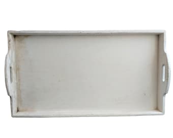 Puede incluir: Una bandeja de servir de madera blanca con bordes ligeramente desgastados. La bandeja tiene una forma rectangular con esquinas redondeadas y dos pequeñas asas a los lados.