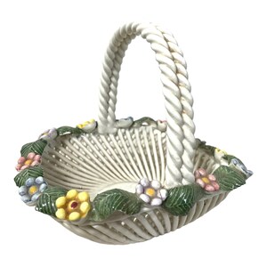 May include: A white ceramic basket with a twisted rope handle and a floral design around the rim. The flowers are in shades of pink, yellow, blue, and green.