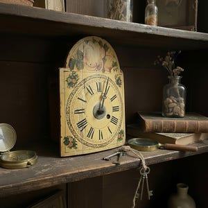May include: A vintage wooden clock with a cream-colored face and black Roman numerals. The clock features floral accents and is displayed on a wooden shelf with other antique items, including books, a compass, and keys. The clock's hands point to approximately 1:50.