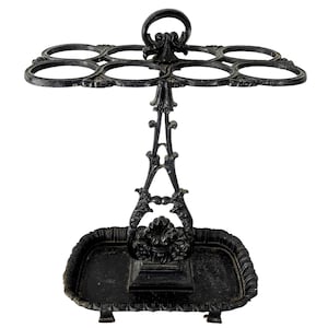 May include: Black cast iron umbrella stand with a decorative design. It has five hooks for umbrellas and a tray at the bottom to catch drips.