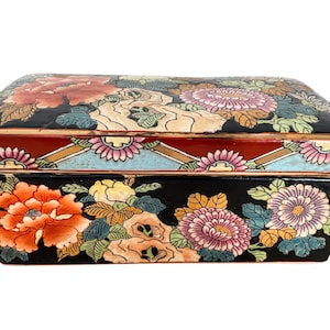 Könnte beinhalten: Eine rechteckige Keramikdose mit schwarzem Hintergrund und einem farbenfrohen Blumendesign. Der Deckel hat ein geometrisches Muster in Rot, Gold und Blau. Die Dose ist mit Blumen in den Farben Rosa, Rot, Gelb und Blau verziert.