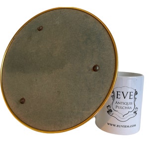 Peut inclure: Un miroir rond &agrave; bordure dor&eacute;e avec un dos en feutre gris. Le miroir est pos&eacute; sur une tasse blanche avec le texte "EVE ANTIQUIS PULCHRA" et le site web "WWW.EUVIEM.COM".
