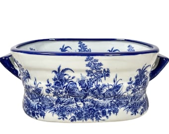 May include: A white ceramic planter with blue floral and bird designs. The planter has two handles and a rounded oval shape.