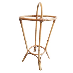May include: A natural woven bamboo plant stand with a round top and three legs. The stand is made of light brown bamboo.