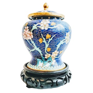 Op de afbeelding: Een blauwe en gouden cloisonné vaas met een bloemenmotief op een houten standaard.