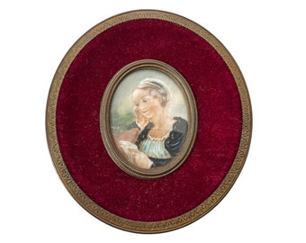 May include: A framed miniature portrait of a woman in a white cap and blue and black dress, set against a red velvet background.