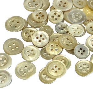 May include: A collection of pearl-like buttons with four holes each. The buttons are various sizes and have a slightly iridescent sheen.