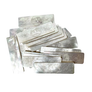 Puede incluir: Una pila de azulejos de nácar blanco con intrincados diseños florales y un motivo de pájaro. Los azulejos son rectangulares y tienen una superficie lisa y pulida.