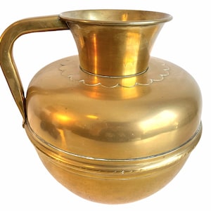 May include: A gold brass pitcher with a round body and a flared top. The pitcher has a handle and a decorative band around the middle.