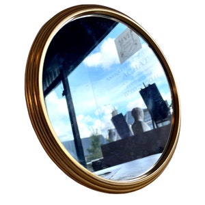 Peut inclure: Un miroir rond avec un cadre dor&eacute; et un bord biseaut&eacute;. Le miroir refl&egrave;te un ciel bleu et une enseigne de magasin qui indique "Antiquit&auml;ten ACHAT" avec un num&eacute;ro de t&eacute;l&eacute;phone.