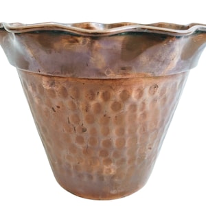 May include: A hammered copper planter with a scalloped rim. The planter is a light brown color and has a rustic look.
