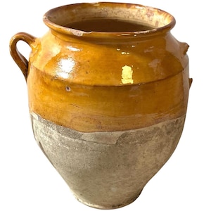 以下が含まれることがあります： 広い開口部と2つの取っ手が付いた、大きなアンティークの陶器の壺。壺は主に温かみのある黄色で、より明るく風化した灰色のベースがあります。表面は光沢があり、経年劣化の兆候が見られます。