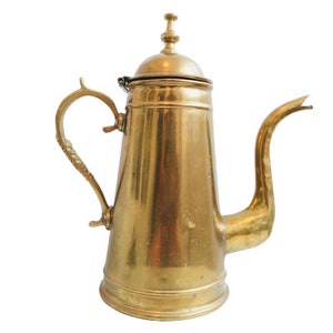May include: A gold-colored brass teapot with a lid and a curved spout. The teapot has a decorative handle.
