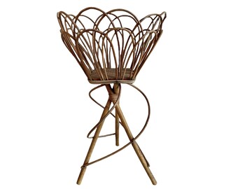 May include: A brown wicker plant stand with a flower-shaped top and three legs. The stand is made of natural materials and has a rustic look.