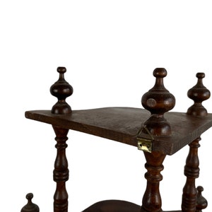 May include: A dark brown wooden shelf unit with three tiers. The shelf has a decorative design with turned wooden posts and finials. The shelf is made of solid wood and has a rustic look.