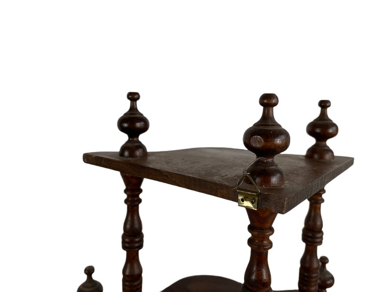 May include: A dark brown wooden shelf unit with three tiers. The shelf has a decorative design with turned wooden posts and finials. The shelf is made of solid wood and has a rustic look.