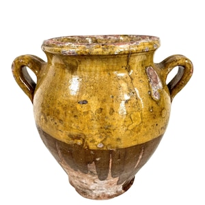May include: A yellow and brown glazed ceramic pot with two handles. The pot has a rustic, antique look and is perfect for displaying flowers or plants.