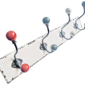 May include: A white wooden wall mounted coat rack with six hooks. The hooks are made of metal and have ceramic knobs in various colors, including red, green, white, and black.