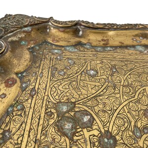 Puede incluir: Una bandeja de metal dorado con un dise&ntilde;o grabado intrincado. La bandeja tiene un borde festoneado y est&aacute; decorada con motivos florales y geom&eacute;tricos.